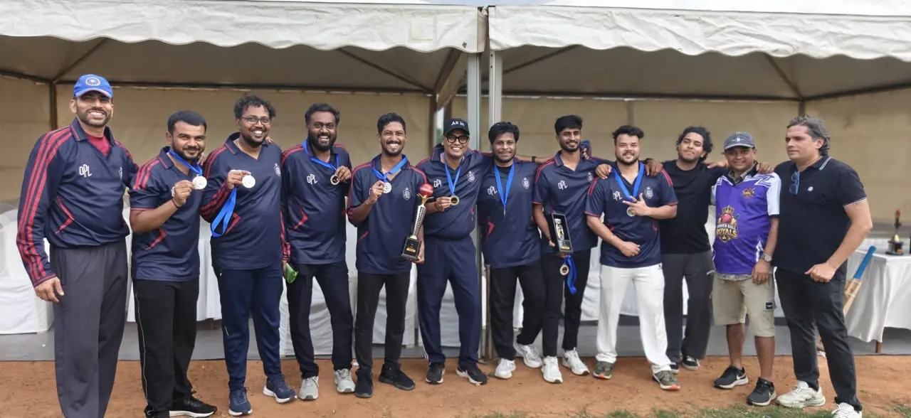 OPL cricket players in navy jerseys with red trim holding medals and a trophy under a tent
