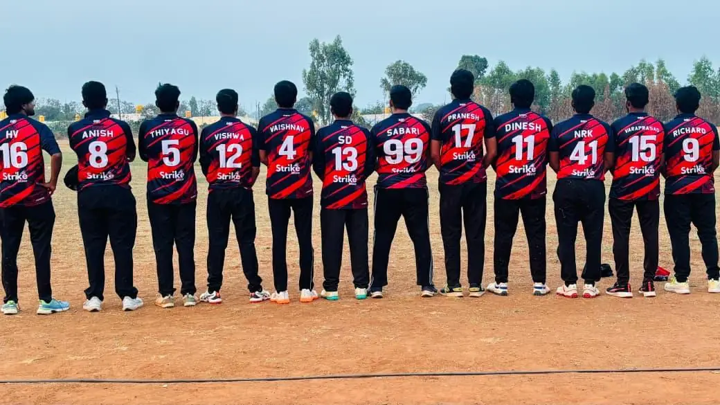 Cricket team lined up from behind in red and black diagonal-stripe jerseys, each with a player name and number on the back and the Strike logo under the number