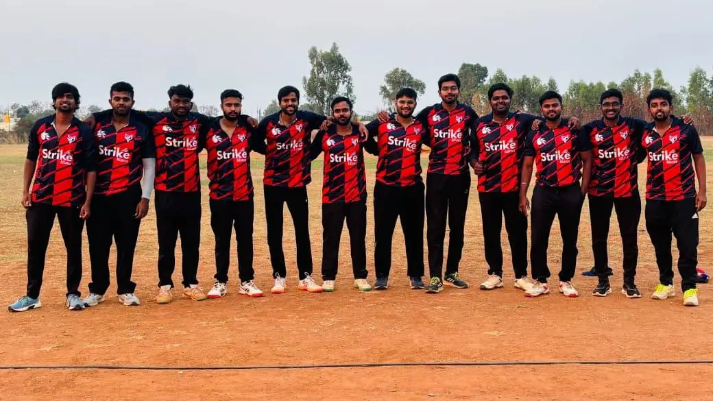 The same cricket team from the front in red and black check jerseys with a wolf crest and the Strike sponsor logo on the chest