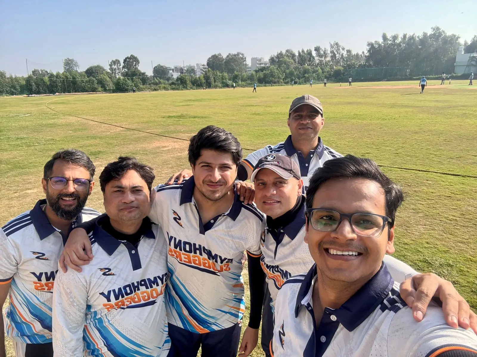 Close-up selfie of Symphony Sloggers players showing the white jersey, navy polo collar and orange team name