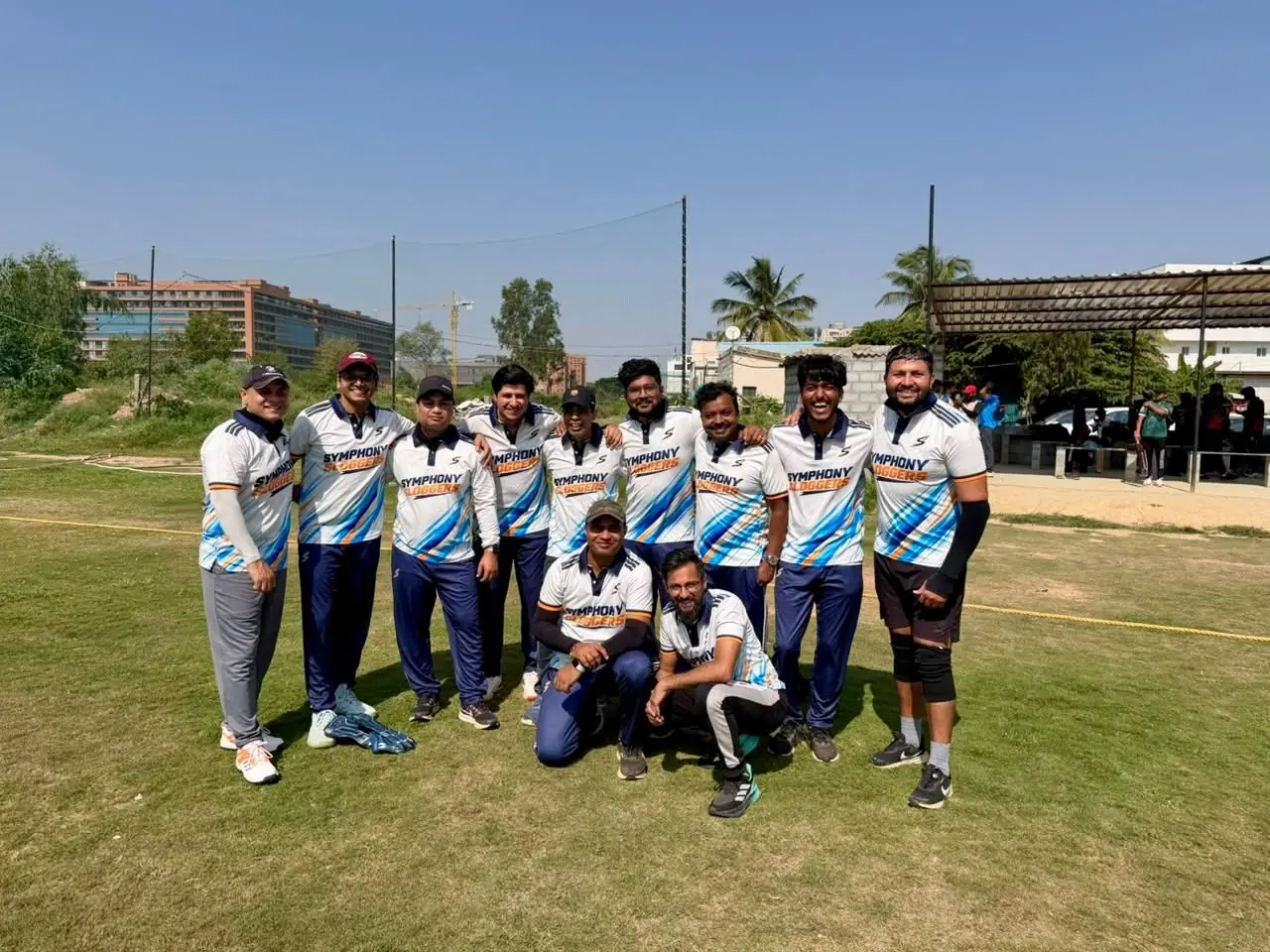Symphony Sloggers cricket team on the ground in white jerseys with blue and orange brush strokes and navy collars